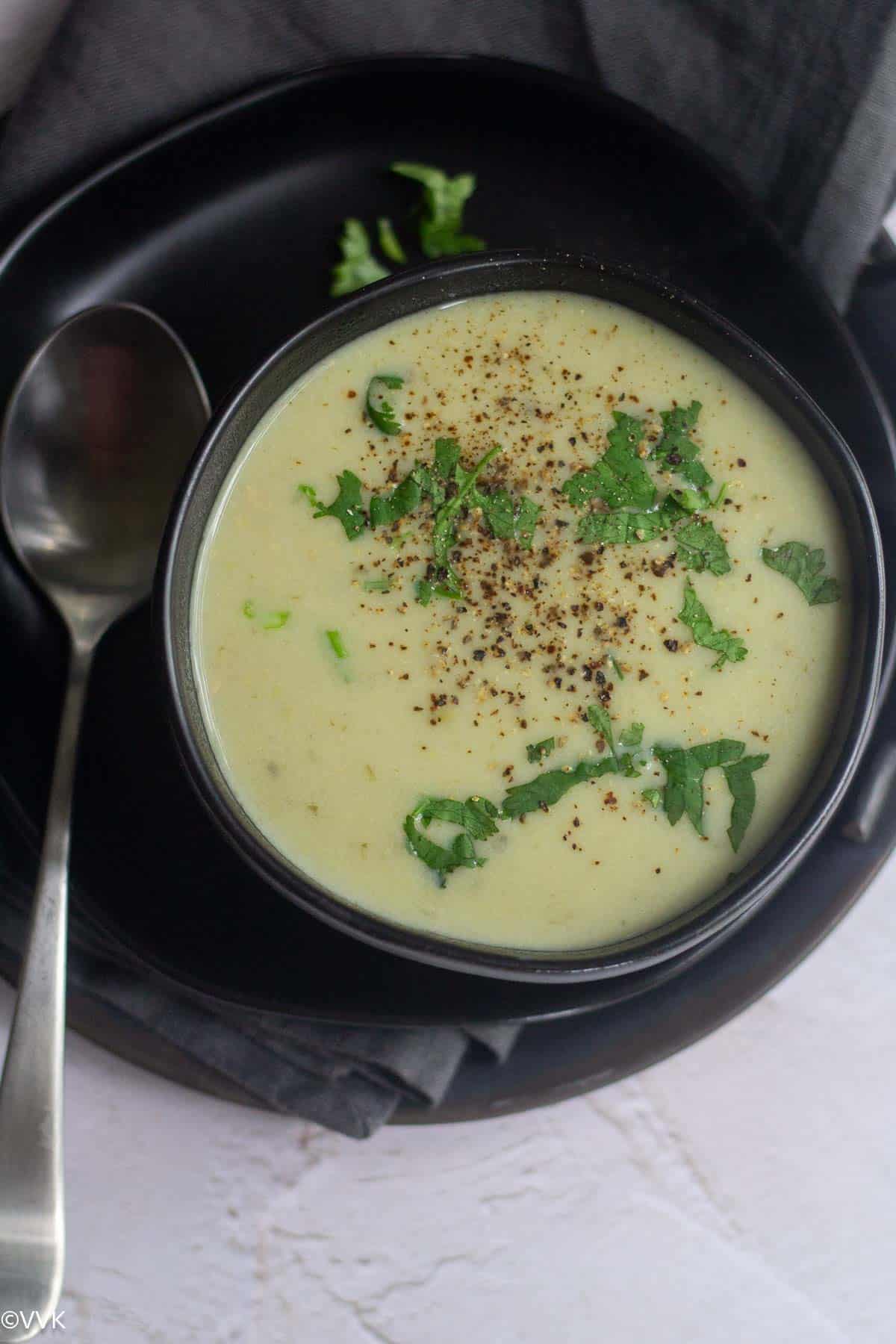 overhead shot of bottle gourd soup served in black bowl with pepper and cilantro sprinkled