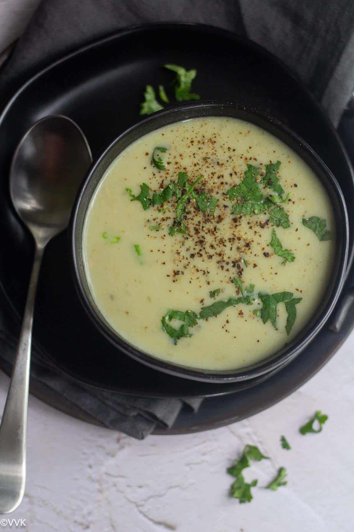 cream of bottle gourd soup served in black bowl with cilantro and black pepper sprinkled